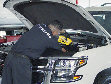 Technician pouring new oil under the hood of a vehicle.