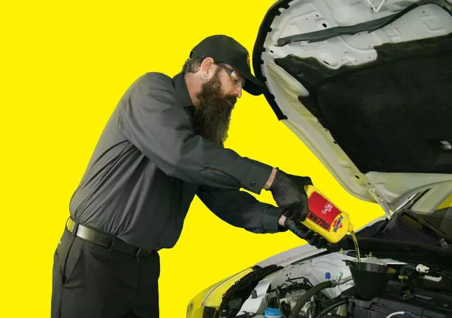 A technician pouring Pennzoil high mileage oil into the top of an engine.