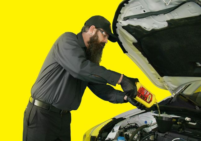 A technician pouring Pennzoil high mileage oil into the top of an engine.