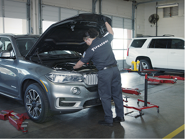 Technician working under the hood of a grey car.