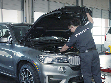 Technician working under the hood of a grey vehicle.