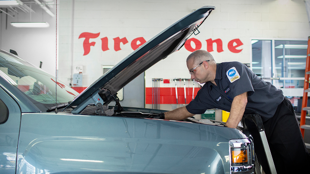 Technician working under the hood of a car in a Firestone shop.