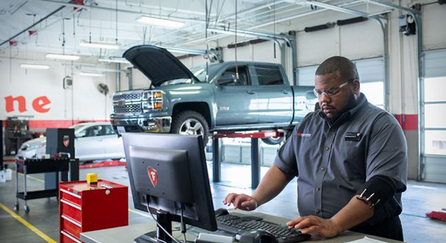 Technican working on a computer with a raised truck in the background in a Firestone shop.