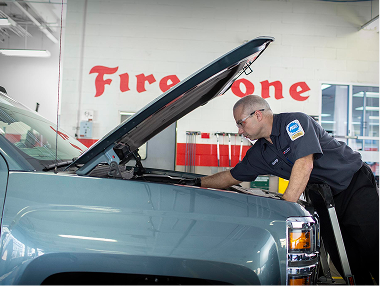 Technician working under the hood of a grey car.