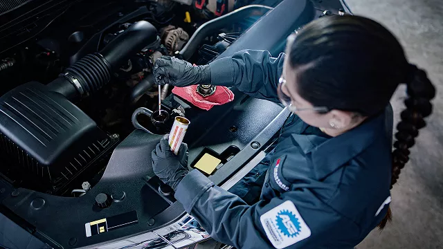 Bird's eye view of a female technician working under the hood of a car.