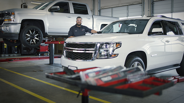 A technician smiling as he stands between two white vehicles in the shop.