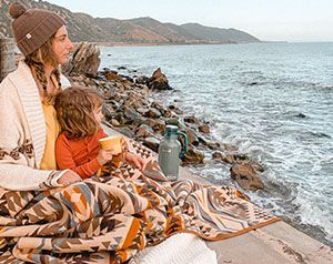 Mother and child sitting in blanket looking at the ocean