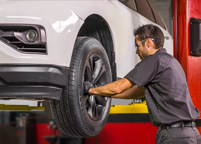 A technician checking the condition of tires for a vehicle raised on a hydraulic lift.