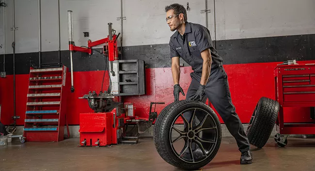 A Tire Plus technician rolls a wheel across the auto shop floor.