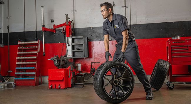 A Tire Plus technician rolls a wheel across the auto shop floor.