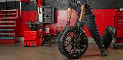 A Tire Plus technician rolls a wheel across the auto shop floor.