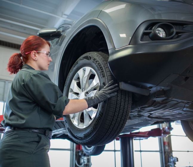 A technician replacing a tire on a raised car.
