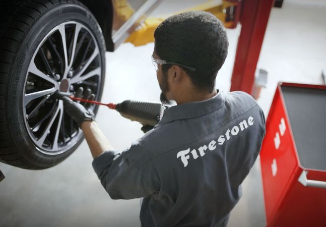 A technician making adjustments to a tire on a raised car.