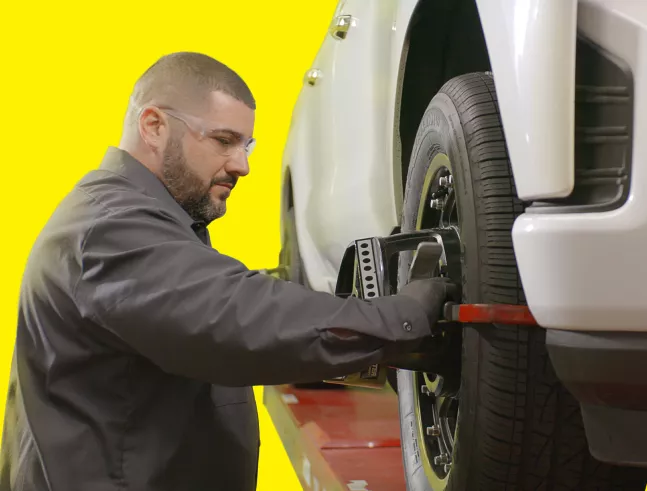 A technician performing a wheel alignment on a vehicle using specialized equipment attached to the tire. 