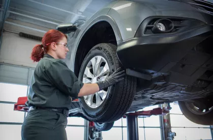 Female technican working on the tire of a raised vehicle.
