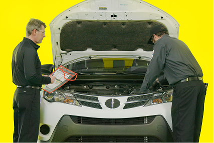 Two auto technicians checking under the hood of a SUV.
