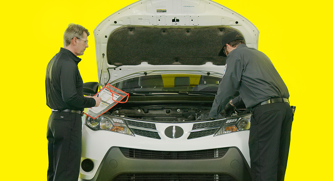 Two auto technicians checking under the hood of a SUV.