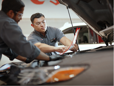 Two technicians working under the hood of a car.