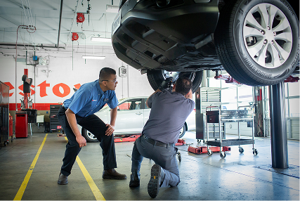 Two technicians working on the wheel of a raised car.
