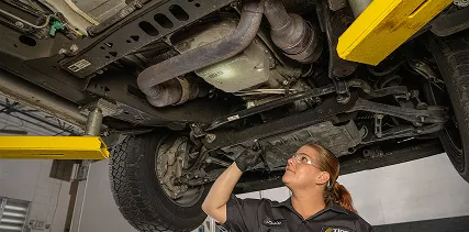 A technician inspecting the chassis of a vehicle that is lifted up in a garage.
