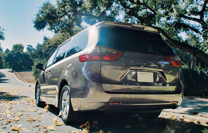 A minivan drives through scattered leaves on a country road.