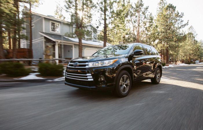 A sleek SUV drives through a wooded neighborhood.