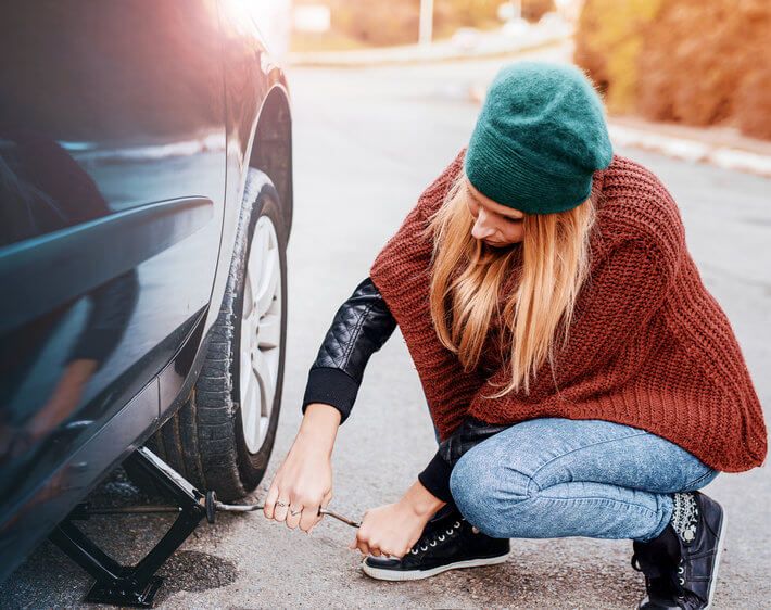 woman using a jack to change a flat tire