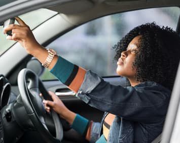 Woman checking rearview mirror in vehicle.