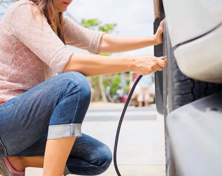 Woman in pink sweater kneeling next to her car tire, filling up tire with air