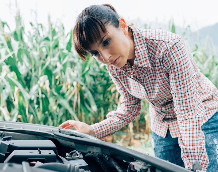 Woman with her ear tilted towards her car's engine, listening for what the car noise might be