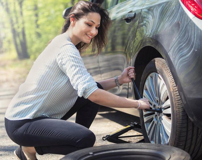 Woman replacing flat tire with spare tire