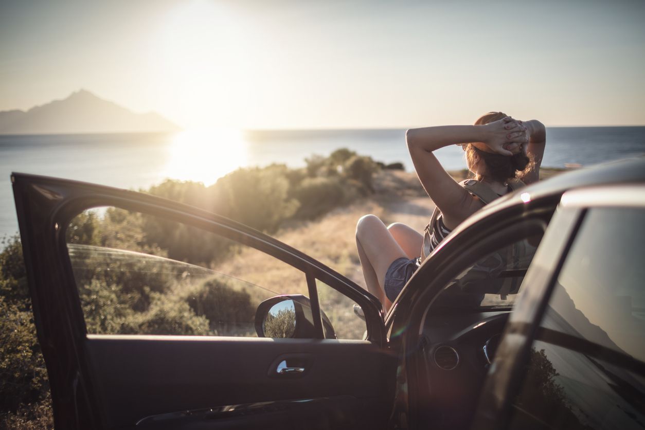 image of woman sitting on her car watching a sunset