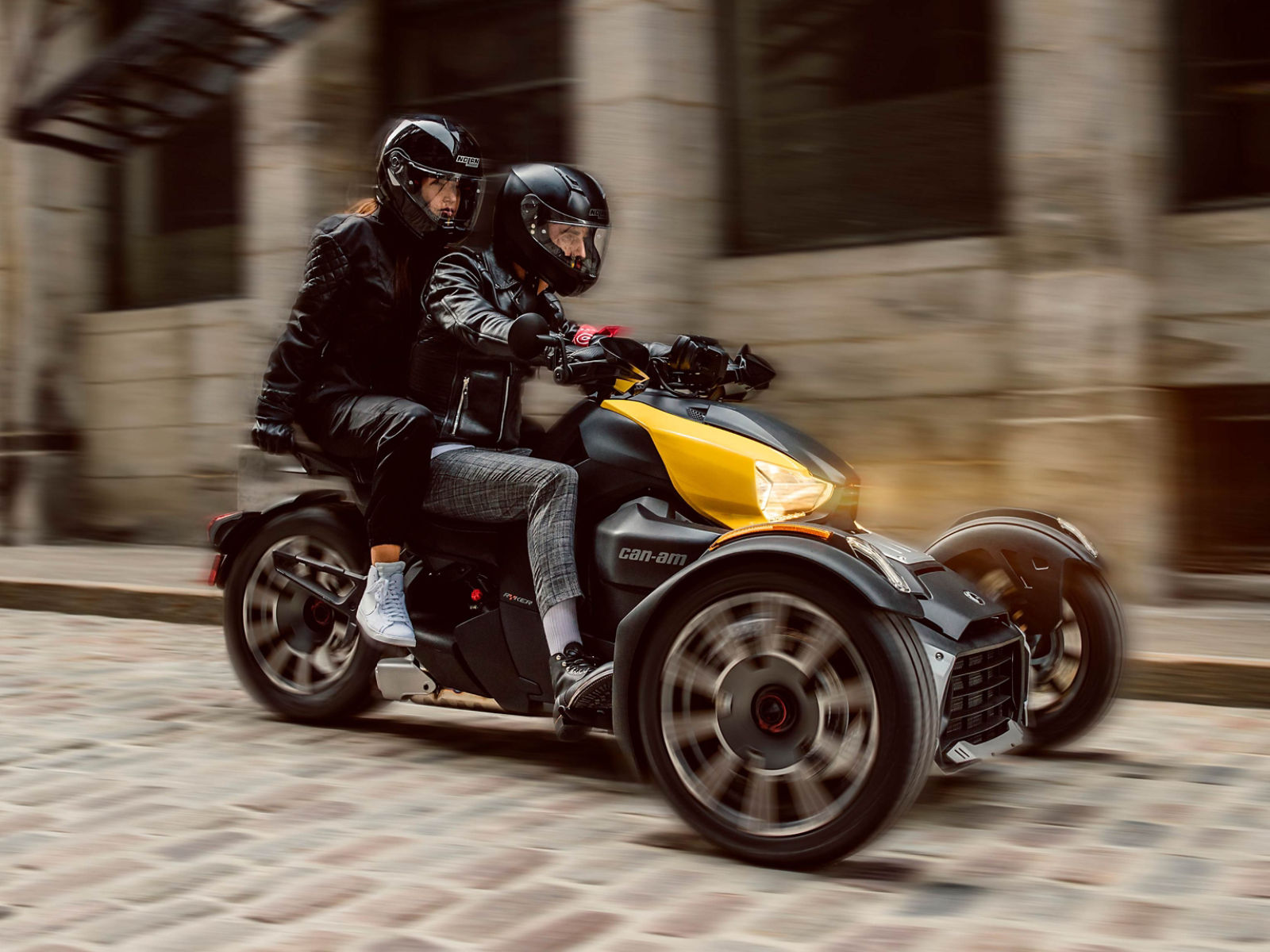 A couple riding a Can-Am vehicle along a narrow cobblestone street