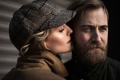 Close up image of bride-to-be in a plaid hat leaning in toward her fiance's cheek
