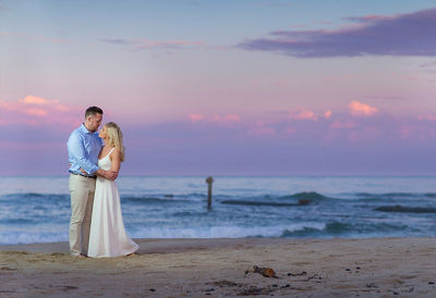 Image of a couple on the beach holding each other with the waves in the background