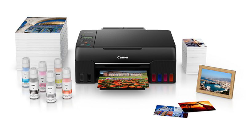  PIXMA G620 - Vue de face à côté de nombreuses piles de prospectus imprimés et d’encres