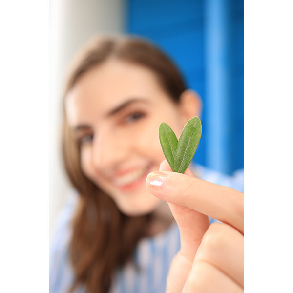  A person holding a small, green leaf close to the camera