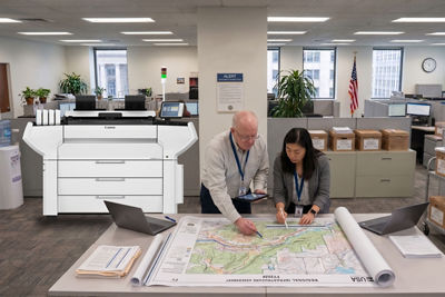 two pepole looking at a map with a Canon printer in the background