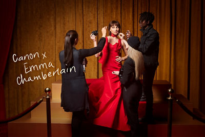 Emma Chamberlain in a Red Dress Standing While Holding A Canon Camera