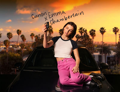 Emma Chamberlain Sitting on a Car While Taking a Picture with a Canon Camera