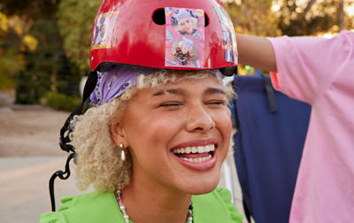 A woman has a large smile while wearing a red helmet with stickers on it