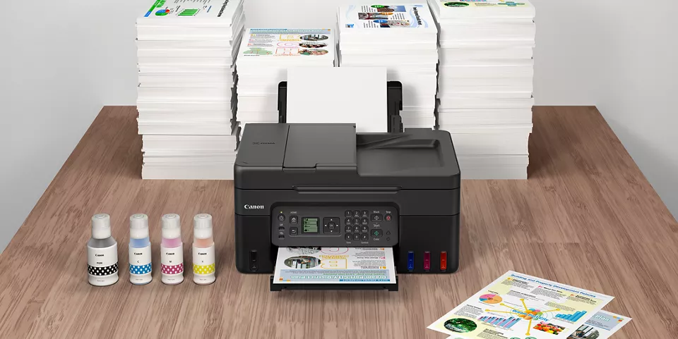The PIXMA G4270 on a desk with a stack of paper behind it the GI-21 Ink bottles to it's left and a small stack of printed papers at the right front of the printer.