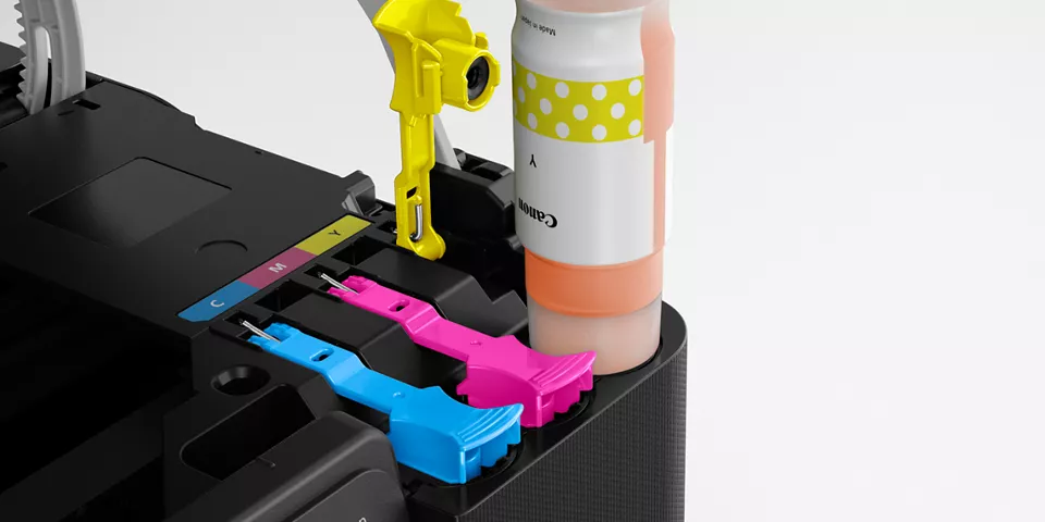 Close-up of the nozzled ink slots while a bottle of yellow ink is refilling the slot
