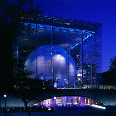 The American Museum of Natural History at night. The building is made of glass and a large model of the universe can be seen inside the building.