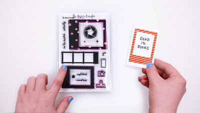 A hand holds a small aspiration card that reads “Read 15 Books” inside an orange stamped border. Next to it is the Captured Stamp Set by The Paper Curator with a hand pointing out the specific frame used to stamp this example card.