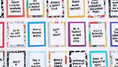 Overhead view of multiple small cardstock aspiration cards arranged in rows. Each card has colorful decorative cardstock borders and a handwritten aspiration in the center, such as “attend a craft club,” “read 15 books,” and “host a dinner party.”