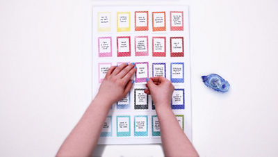 Hands placing an aspiration card onto the bingo board using archival adhesive.