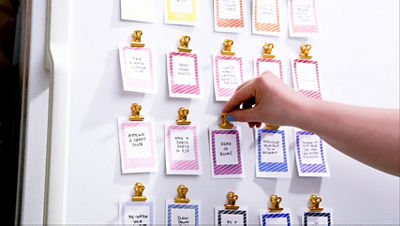 A grid of aspiration cards is mounted to a white refrigerator surface using small gold magnetic clips.