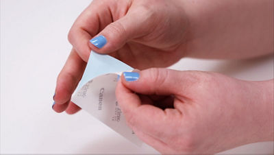 Close-up of hands removing the backing from a small printed photo sheet, revealing the adhesive backing used to attach the photo to the bingo board.