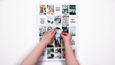 Overhead view of hands placing a small printed photo onto the bingo board grid, replacing the written card with the photo to mark the aspiration as completed.